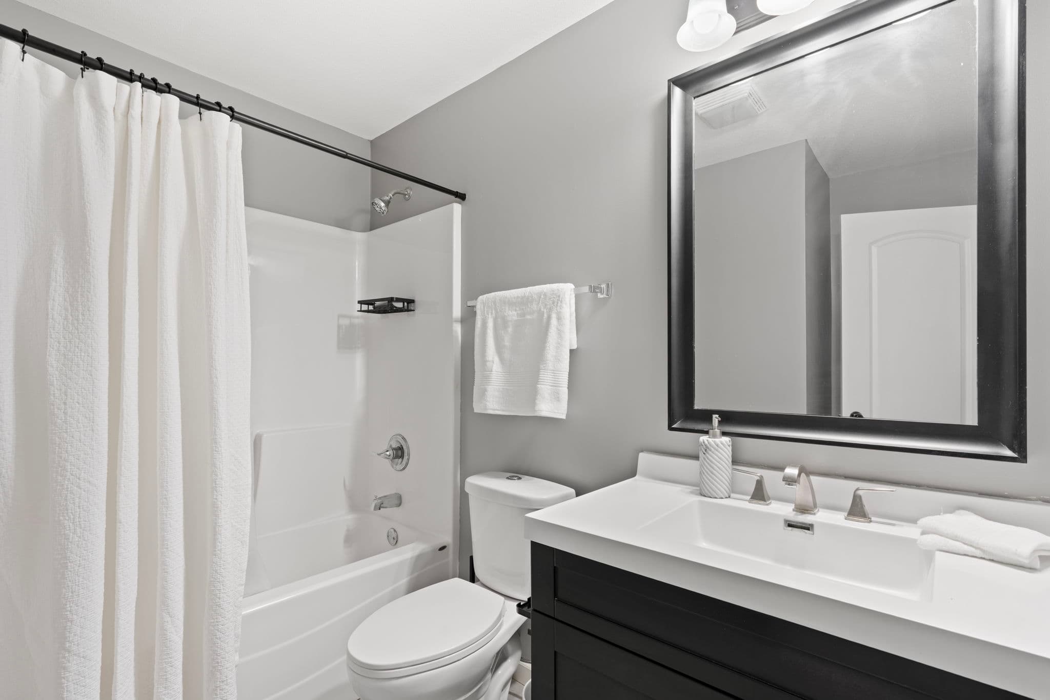 Second full bathroom with single-sink black vanity and tub-shower